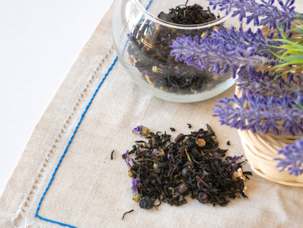 草药茶与蓝色干花在圆玻璃花瓶茶散布在桌子和亚麻布餐巾。薰衣草花图片下载