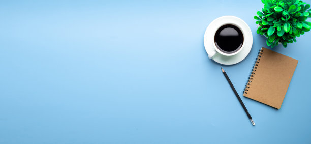 平铺，俯视图办公桌书桌。工作空间，笔记本电脑，办公用品，铅笔，绿叶，和咖啡杯的蓝色背景。图片下载