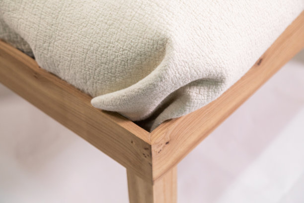 手工制作的乳白色毛毡枕头放在木制床头柜上，背景是白色的图片下载