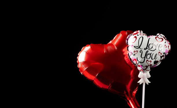 红色的心形气球和白色的心形气球，上面印着“我爱你”和心形图案，在黑色背景上，选择聚焦在白色气球上。图片下载
