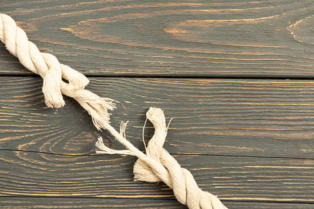 灰色木头背景上一根即将断裂的绳子。差距。图片下载