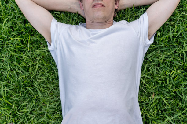 穿着仿白色t恤的男子躺在草地上。模板时尚设计拷贝空间图片下载