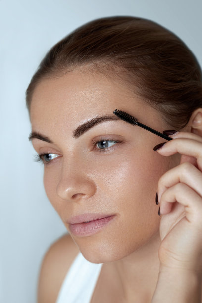 眉毛化妆：美女用眉刷塑造眉形特写。美妆模特用专业化妆勾勒眉毛图片下载