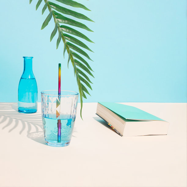 玻璃里的冷蓝色饮料和绿色棕榈枝下的淡蓝色书。模仿海滩夏日的棕榈树阴影。美学抽象的设计理念。阳光沙滩日的概念。图片下载