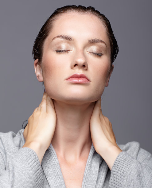 年轻女子的肖像在灰色连衣裙与手在脖子上。深色皮肤的女孩，闭着眼睛，化着日间女性妆图片下载