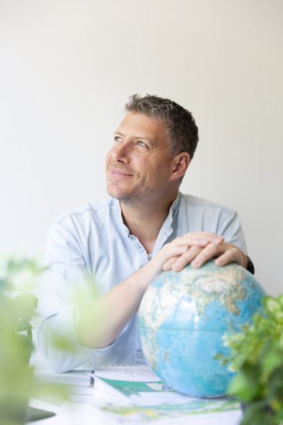 环境工程师坐在他的工作桌旁，手里拿着地球仪，周围是植物的商业肖像图片下载