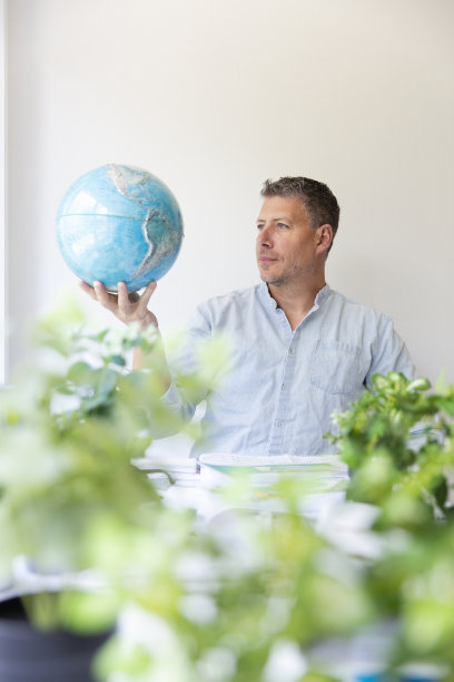 环境工程师坐在他的工作桌旁，手里拿着地球仪，周围是植物的商业肖像图片下载