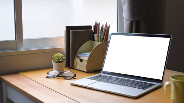 笔记本电脑，眼镜，咖啡杯和木桌上的用品。空白屏幕显示图形蒙太奇。图片下载