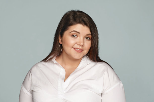 迷人的大码年轻女性的照片，黑色松散的头发和大曲线的身体微笑，表达喜悦和积极的情绪，穿着白色正式xxl衬衫孤立的姿势图片下载