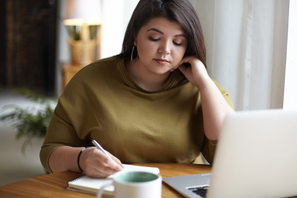 有吸引力的集中的大尺寸年轻的自我雇佣女性曲线身体在家远程工作，在抄本上做笔记，计划商业约会。通讯、技术和小工具图片下载