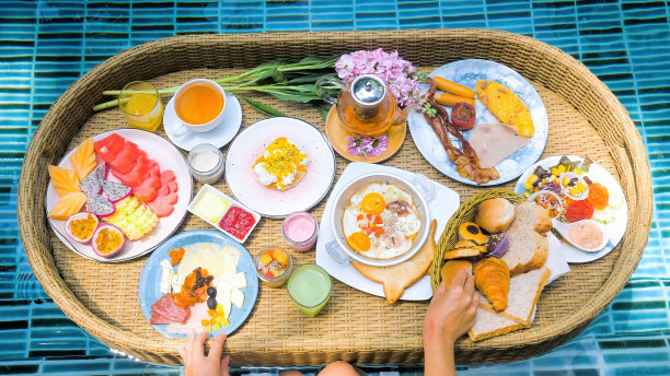 丰富多彩的早餐或午餐与女人的手在浮动托盘在游泳池图片下载