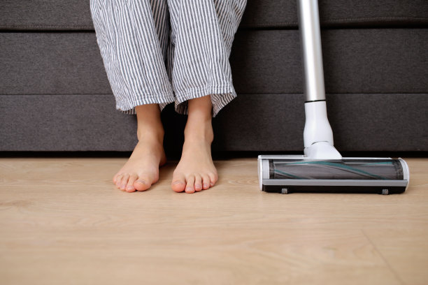 年轻女子带着可充电吸尘器坐在家里的沙发上。图片下载