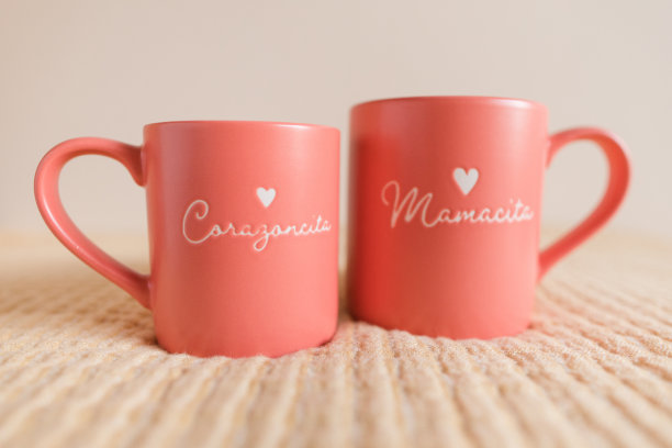 一个母亲和女儿的手拿着粉红色的杯子，上面写着“Mamacita”和“Corazoncita”，西班牙语是可爱的“妈妈”和“小爱”的意思。图片下载