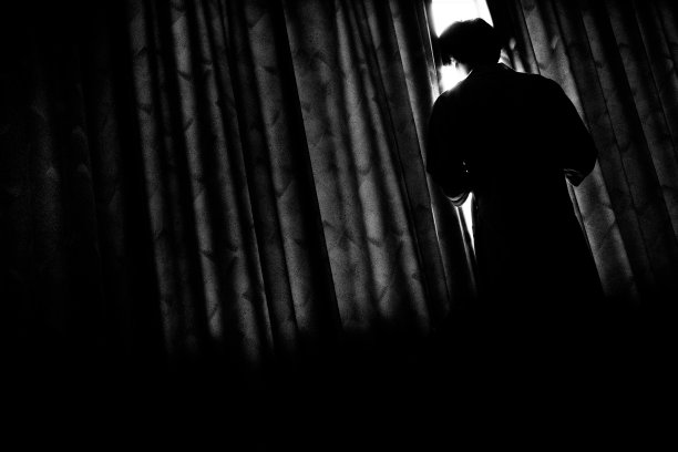 一个人的形象，通过一个缺口在一个黑暗的房间窗帘，单色图片下载