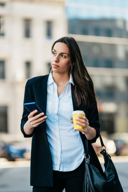年轻的女商人在街上用她的智能手机图片下载