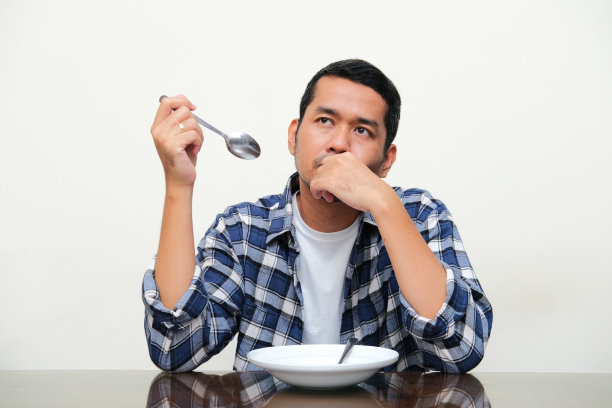 亚洲成年男子坐在空盘子前，表情困惑图片下载