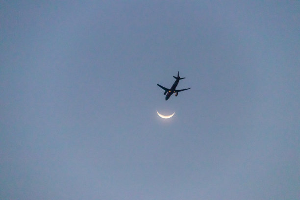在蓝天背景下，飞机在月亮附近飞行。美丽神秘的月亮与飞机在傍晚的日光。图片下载