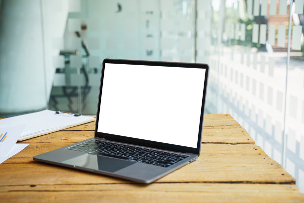 笔记本电脑与空白白色屏幕在木制桌子蒙太奇你的广告。图片下载