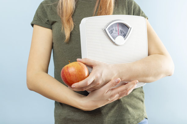 蓝色背景上，一个女人拿着体重秤和红苹果。健康饮食的概念。饮食图片下载