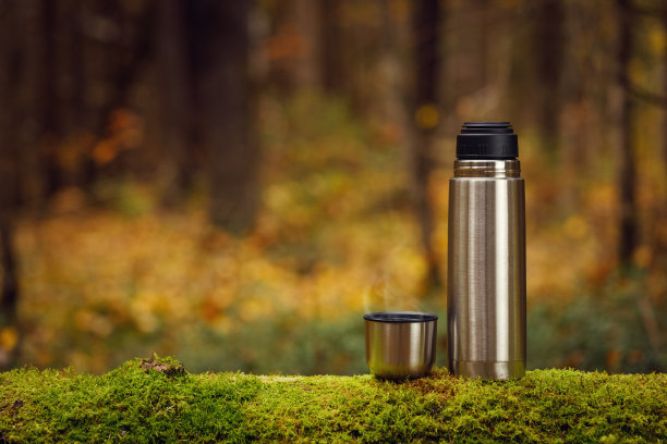 聚焦在一棵长满青苔的老树上，有一个钢制保温瓶，里面放着美味的热茶。图片下载