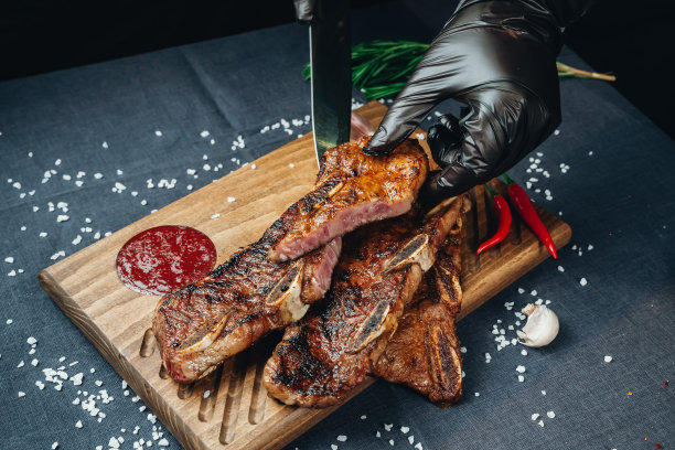 一个男厨师的手戴着手套用刀切多汁的牛排的特写。用木盘子盛食物图片下载