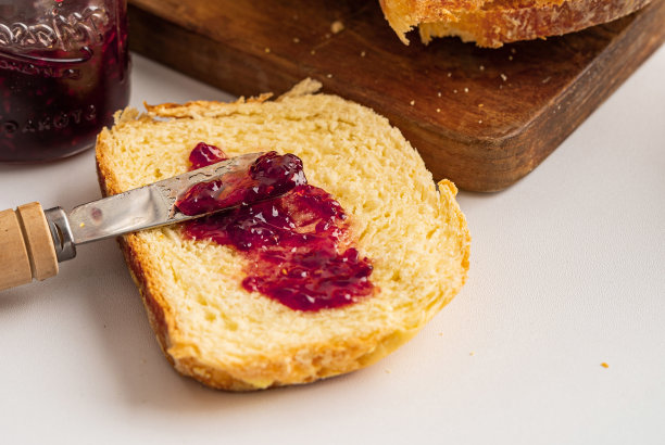 一块涂着蓝莓酱的面包，上面放着一把刀，白色的背景上，后面放着一块棕色的砧板图片下载