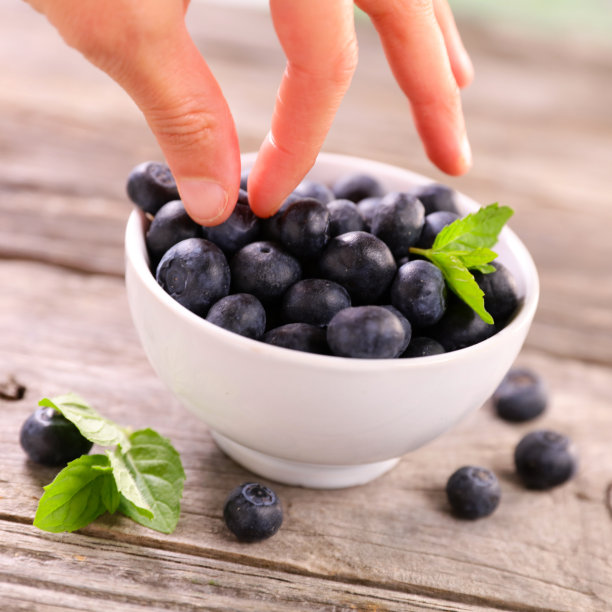 一碗新鲜的蓝莓水果，手里拿着一个蓝莓图片下载