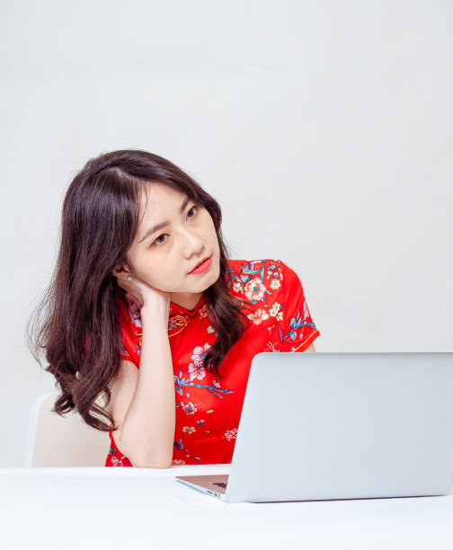 一个年轻的亚洲女人在传统旗袍旗袍肖像使用笔记本电脑在白色背景。图片下载