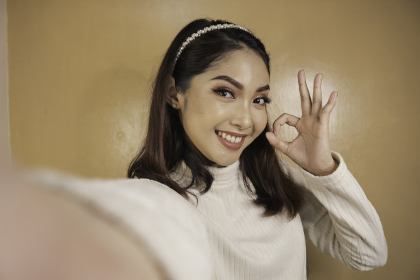 年轻的亚洲女子是自拍与快乐的笑脸和ok sign on嘴附近看相机图片下载