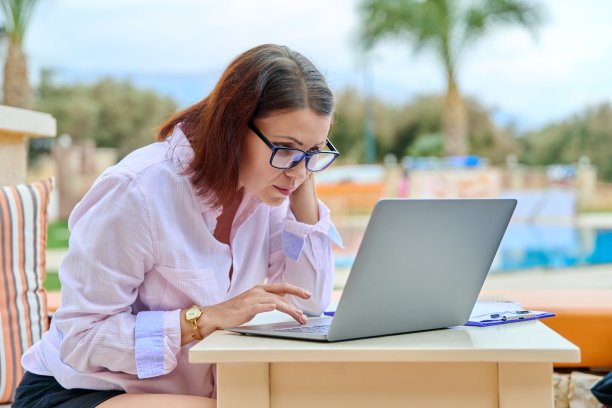 成熟的商业女性坐在室外游泳池旁，用笔记本电脑工作图片下载