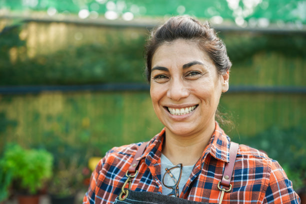 在温室花园里工作的拉丁妇女在镜头前微笑-关注脸部图片下载