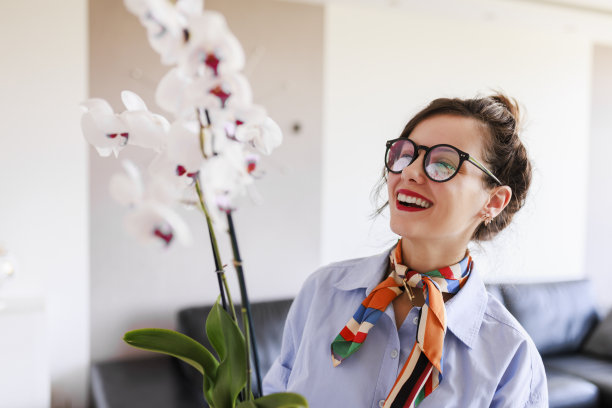 家庭主妇照料着家里的花草，五颜六色的蝴蝶兰。照顾家庭植物的女人。捧着白花的园丁图片下载