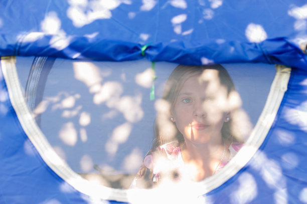 女孩舒适地坐在蓝色露营帐篷内的防蚊纱窗后，向外看，少女肖像，清晨图片下载