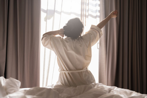 白色连衣裙亚洲女性美女伸展早晨醒来清新和无忧无虑的周末时刻在舒适的室内卧室与白色窗帘和阳光背景的生活方式的家概念图片下载