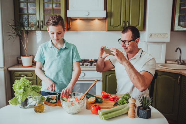 父亲和儿子在家做饭，为社交网络上的博客录制视频。隔离和自我隔离期图片下载