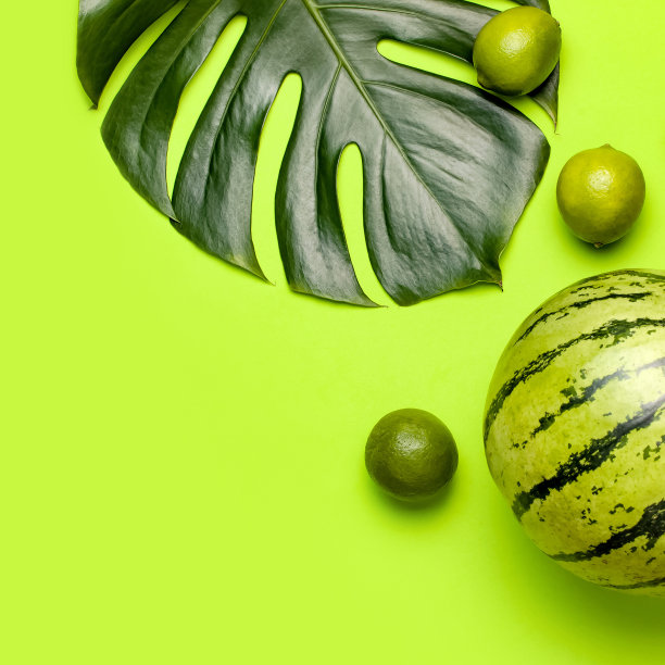 成熟的西瓜浆果，整个酸橙，热带叶monstera在绿色背景俯视图平铺。绿色条纹整西瓜。夏天明亮的背景。最小水果概念图片下载