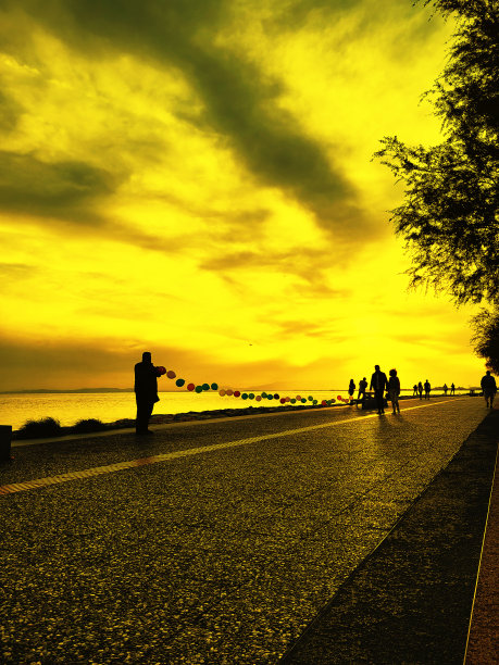 五颜六色的玩具气球在一根绳子上排列，人们在海滩上休闲活动的剪影图片下载