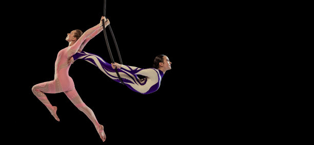 两个年轻女孩的肖像，专业的空中体操运动员表演的铁环孤立在黑色的工作室背景。摩天观景轮图片下载