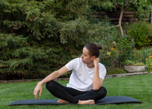 在大自然中，十几岁的男孩在花园或公园户外的瑜伽垫上盘腿望向一边图片下载
