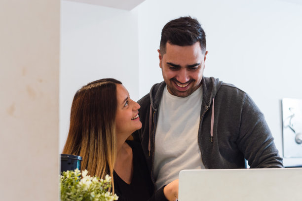 年轻女子微笑着看到她的丈夫在使用笔记本电脑，对他们的数字业务感到高兴图片下载