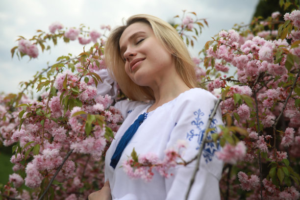 年轻的金发女子在花园里欣赏盛开的樱花。图片下载