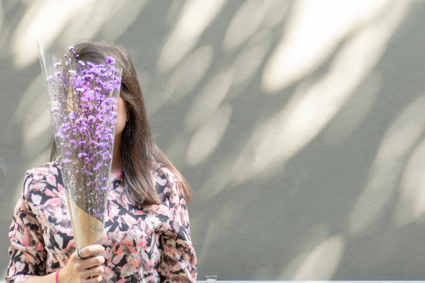 亚洲女子拿着一束紫色的花，花朦朦胧胧的脸，水泥墙的背景。图片下载