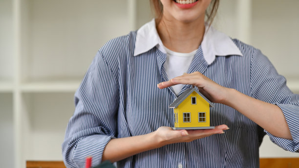 微笑的年轻女子手牵房子模型。新房子，保险和房地产的概念。图片下载