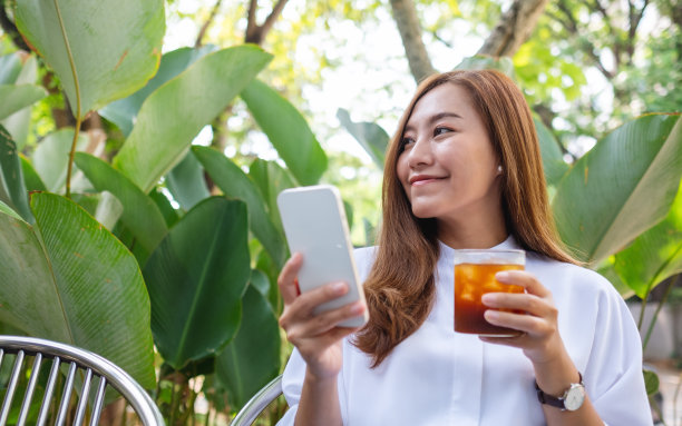 一个美丽的年轻女人在户外喝咖啡时手持和使用手机的肖像图像图片下载