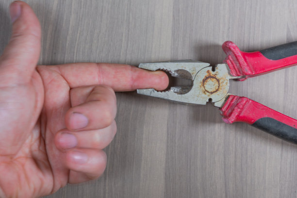 木质背景上的各种工具：钳子夹着手指图片下载