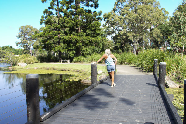 金发女子站在码头上，眺望着湖水和树木。周围都是绿色的树。蓝色上衣，蓝色牛仔短裤。澳大利亚昆士兰黄金海岸图片下载