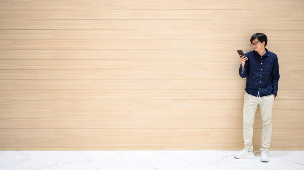 一名亚洲男子在木墙旁使用智能手机图片下载
