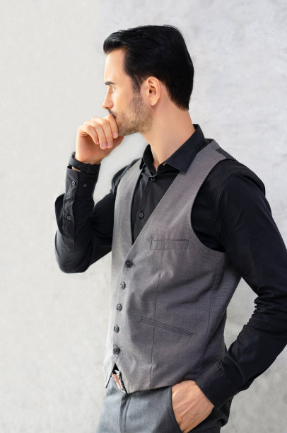 有思想的英俊年轻人的肖像胡子，穿着正装，手放在下巴上，看着别处，而站在灰色的背景。图片下载