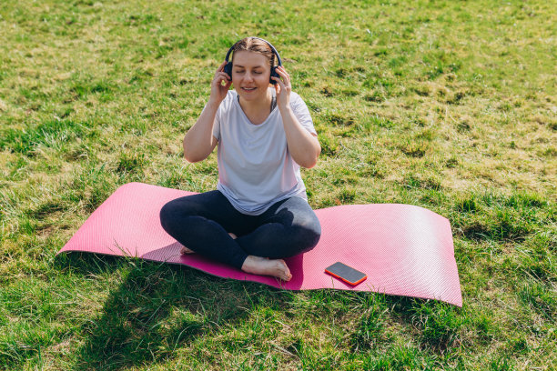 美丽的年轻红发女人放松与智能手机在瑜伽垫上训练后。快乐的女孩戴着耳机听音乐。运动或瑜伽的概念图片下载