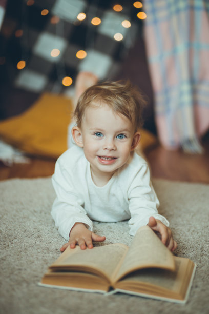 可爱的宝宝在毯子和花环做成的房子或城堡里看书。图片下载